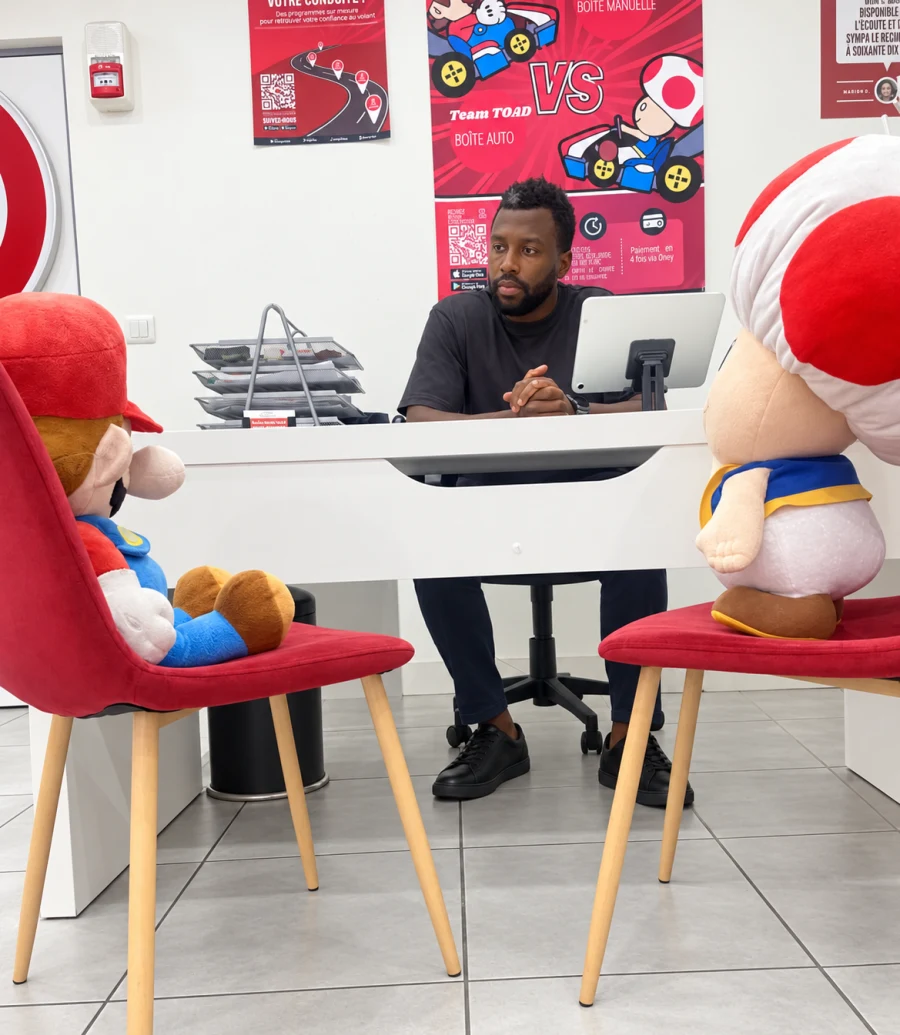 Un enseignant d’Appui Permis assis à son bureau fait face aux peluches de Mario et de Toad, installées sur deux chaises